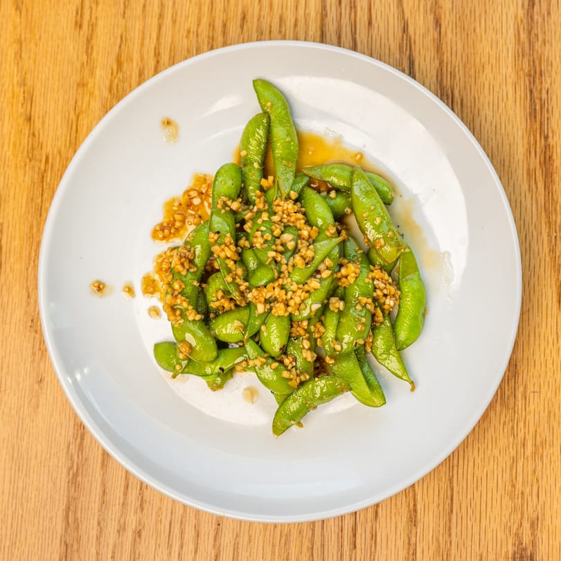 Edamame pods with garlic and sauce on a white plate at Restaurant Tatsuki.