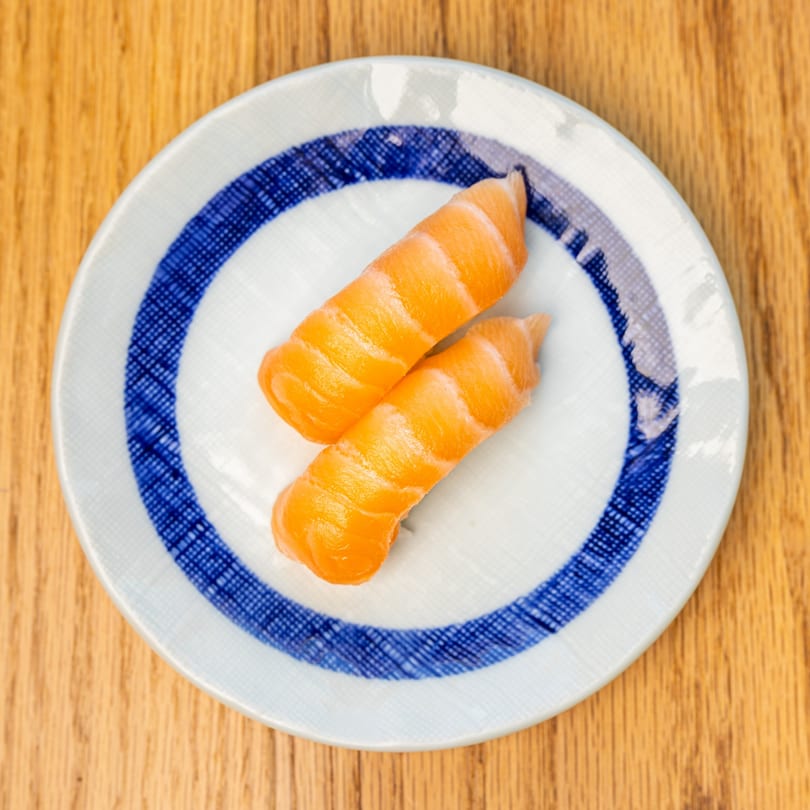 Two pieces of salmon nigiri sushi on a white plate with blue stripes, on a wooden table.