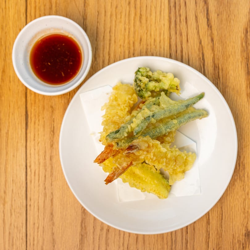 Assorted tempura, including shrimp, green beans, and broccoli, with a side of dipping sauce.